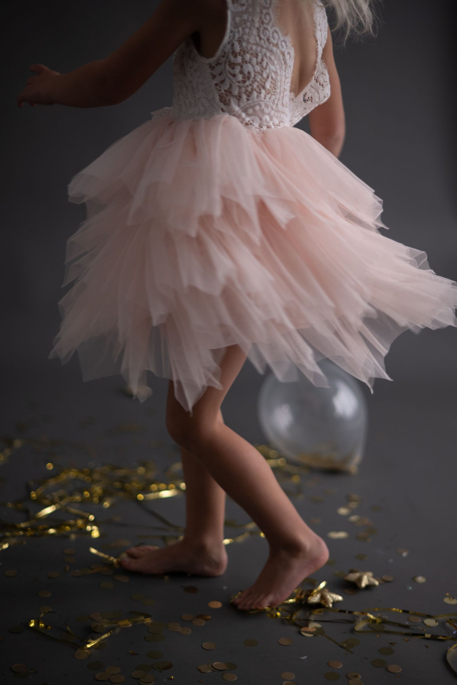 A young child in a pink tulle dress dances joyfully against a dark backdrop with glowing golden bokeh lights.