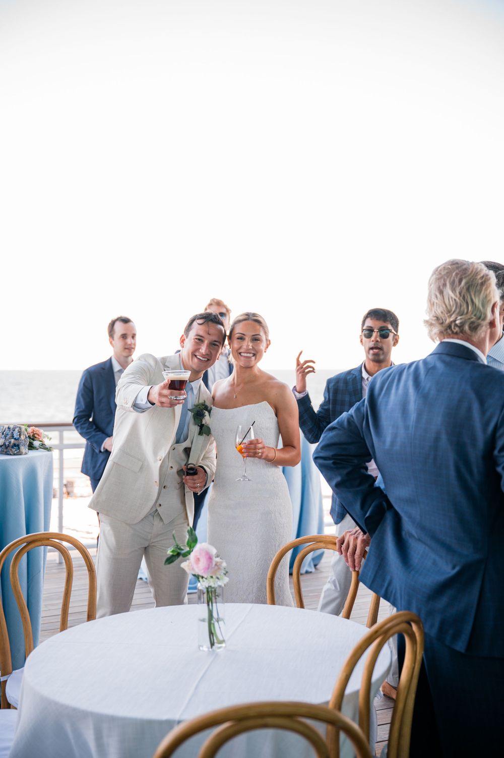 Wedding guests laughing and socializing at round tables with white tablecloths and wooden chairs.