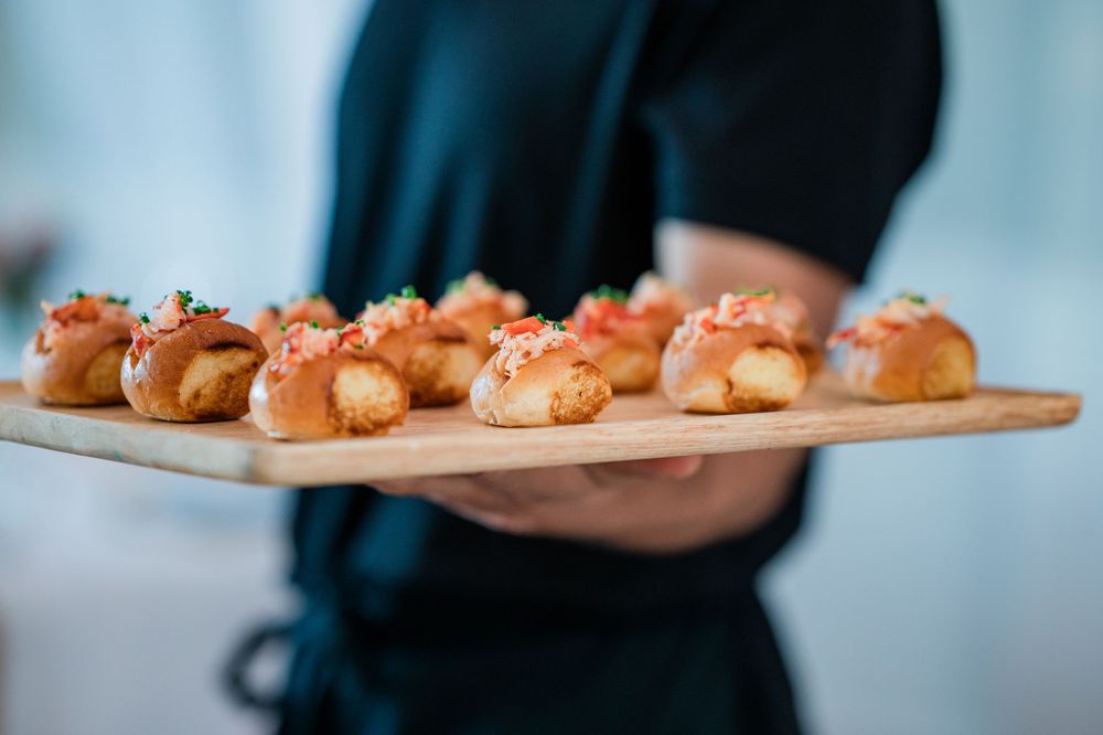 Hands holding wooden serving boards with rows of freshly baked pastries in a restaurant setting.