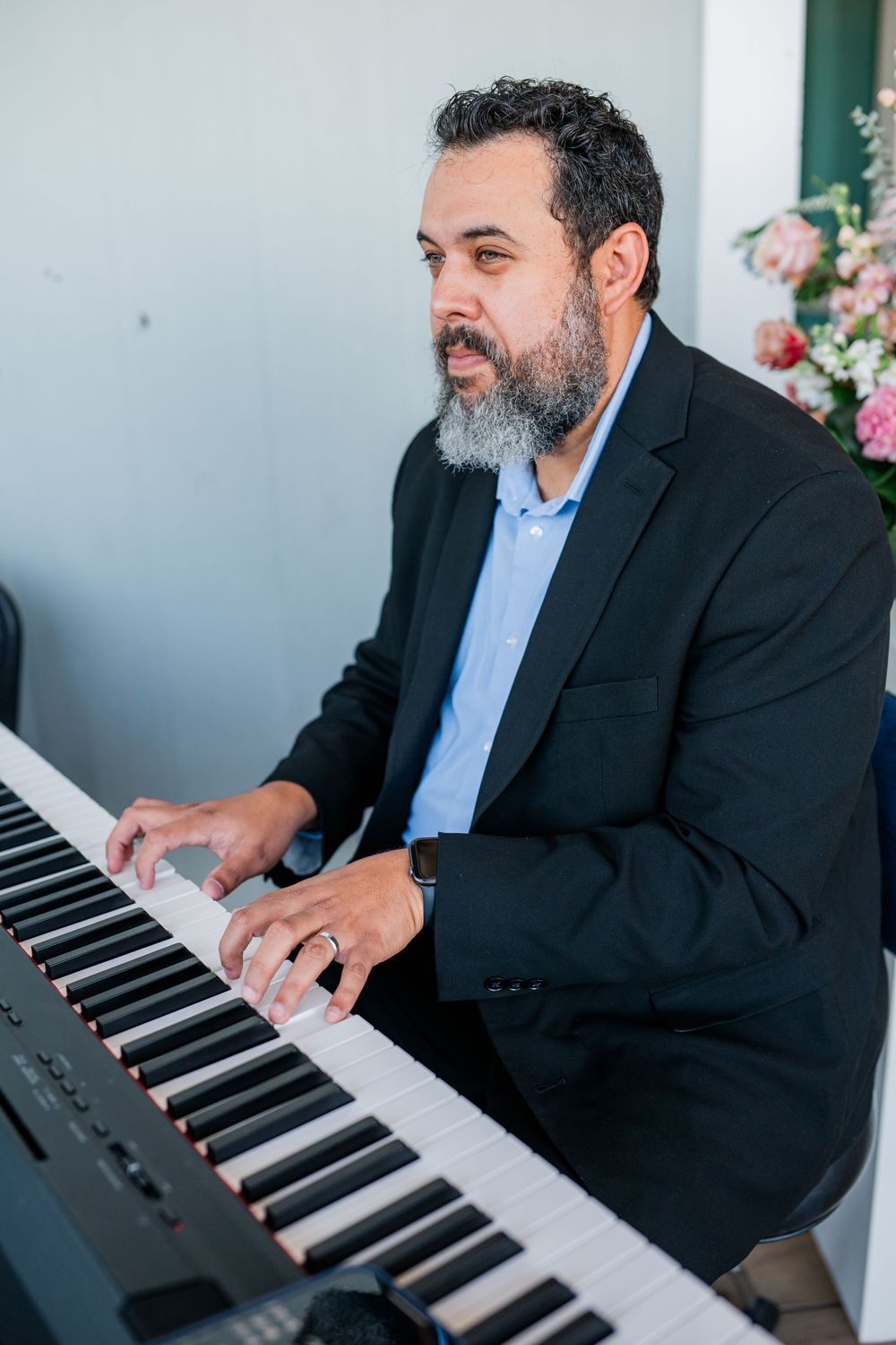 Musician playing piano keys at an event with flowers in background.