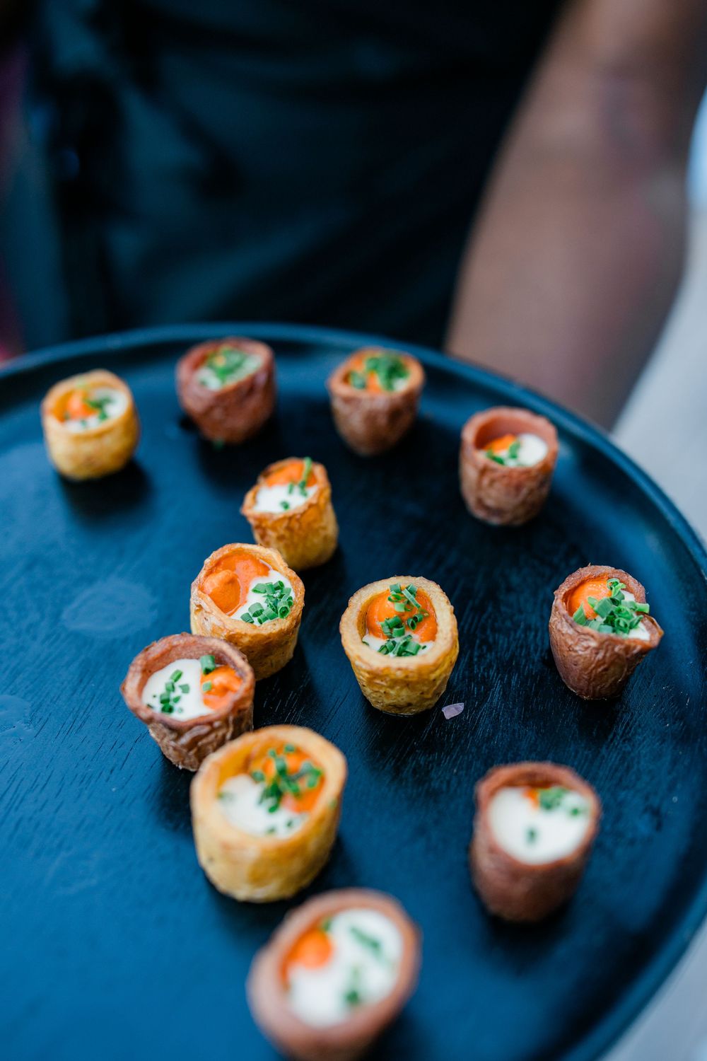 Small appetizers garnished with herbs served on dark plates at an elegant event.