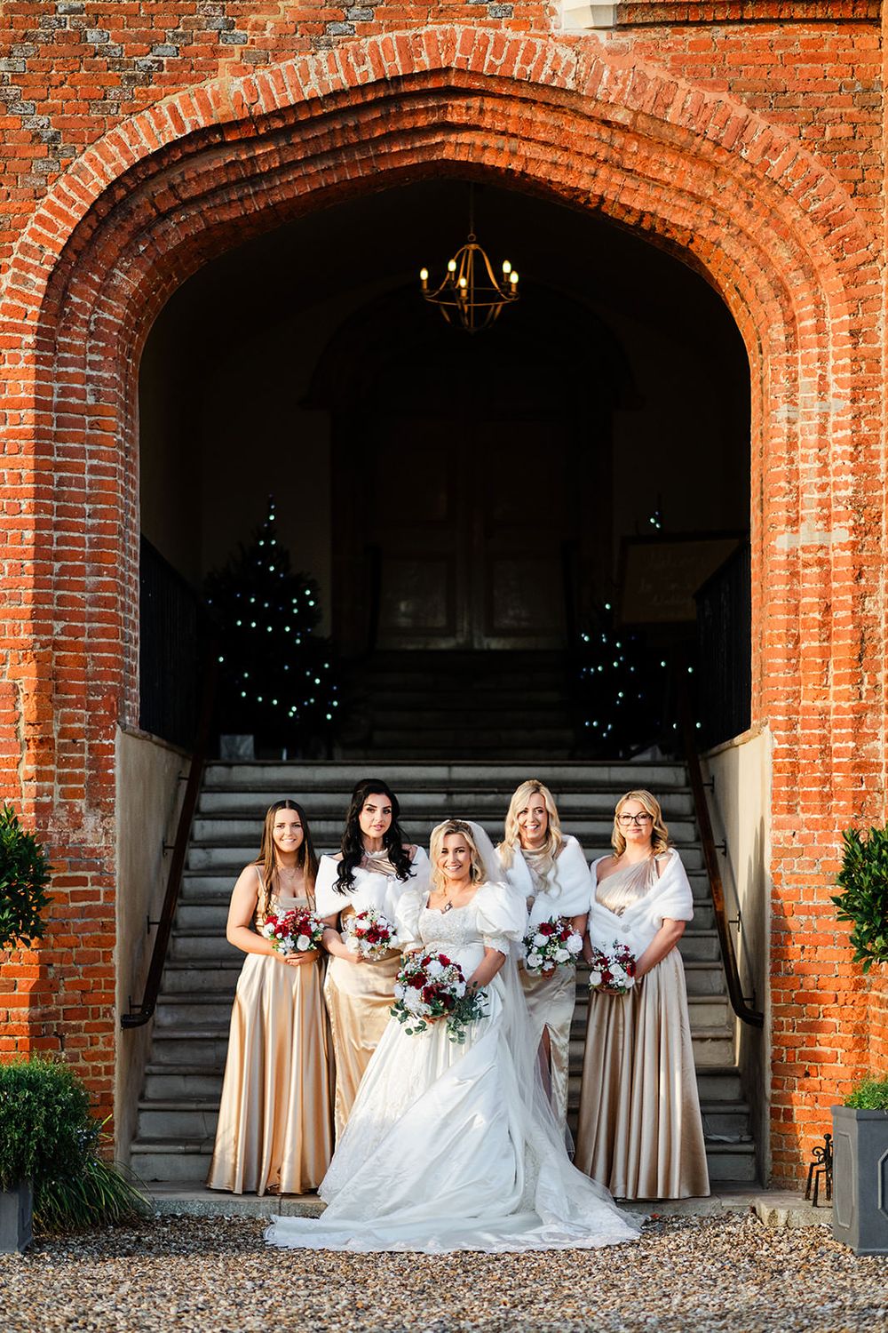Wedding party poses under rustic brick archways at a historic venue with elegant beige bridesmaid dresses.