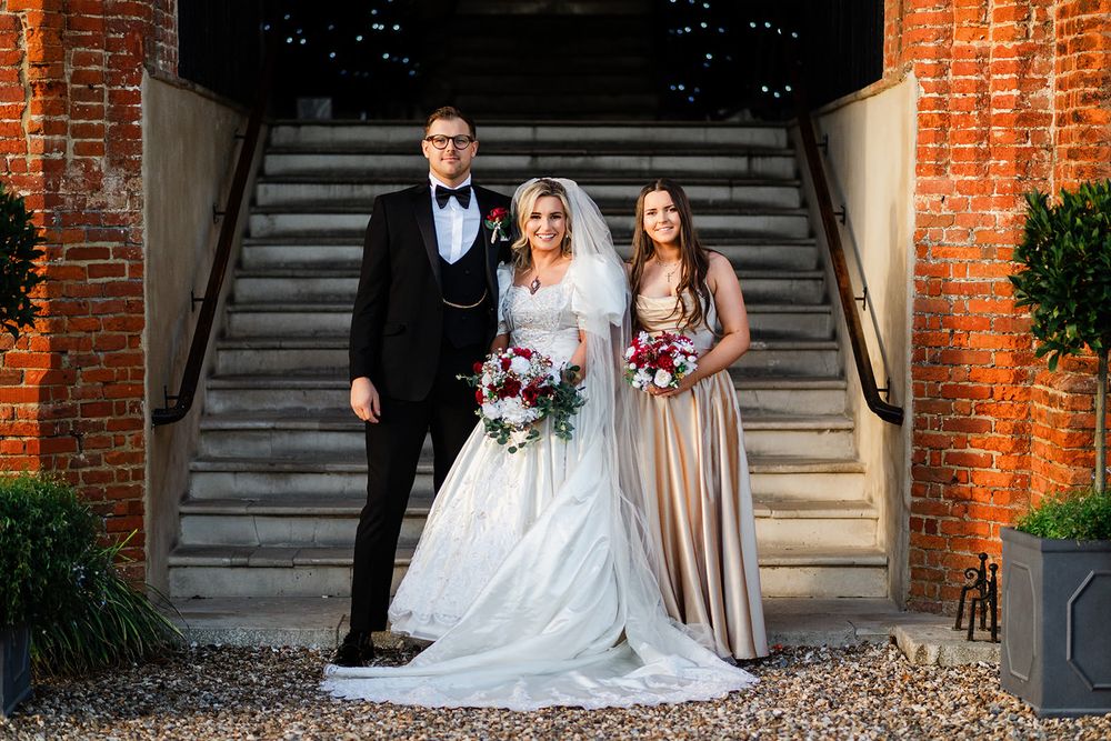 A wedding party poses on grand stone steps between rustic brick walls at an elegant venue.