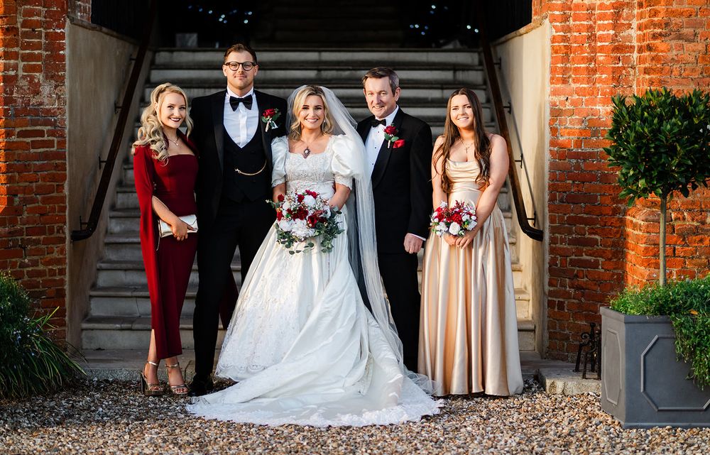 Wedding party poses under brick archway at elegant venue during formal celebration.