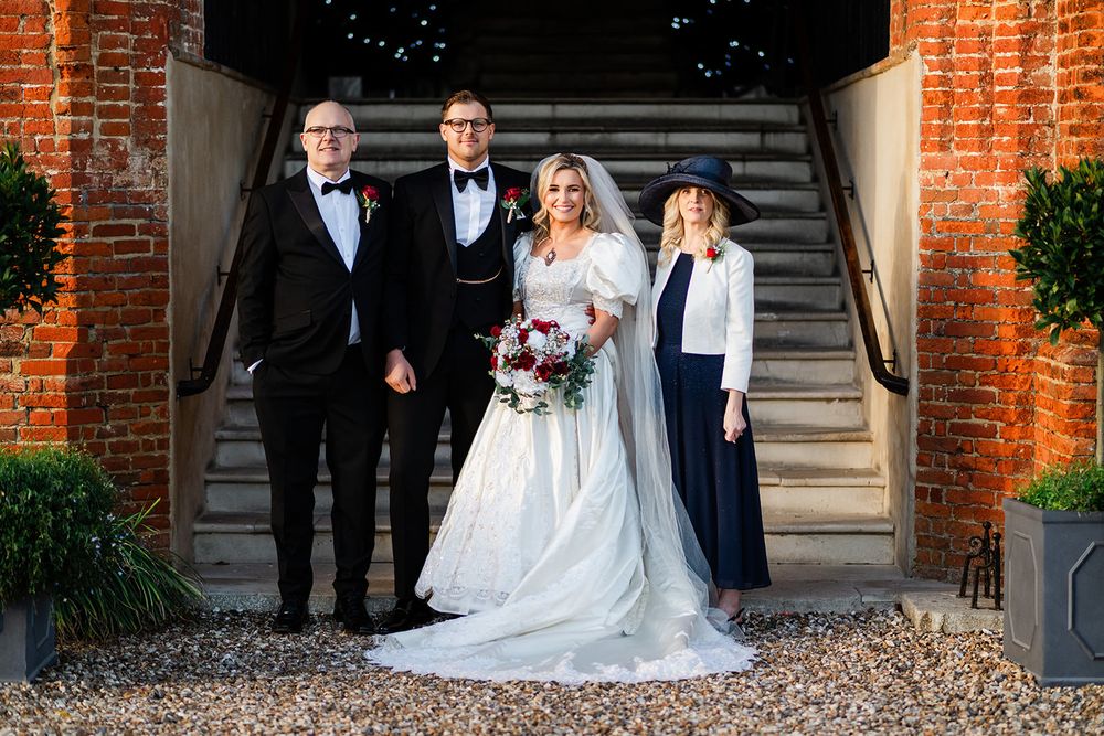 Bride and groom pose with wedding party on brick steps at elegant venue during golden hour.