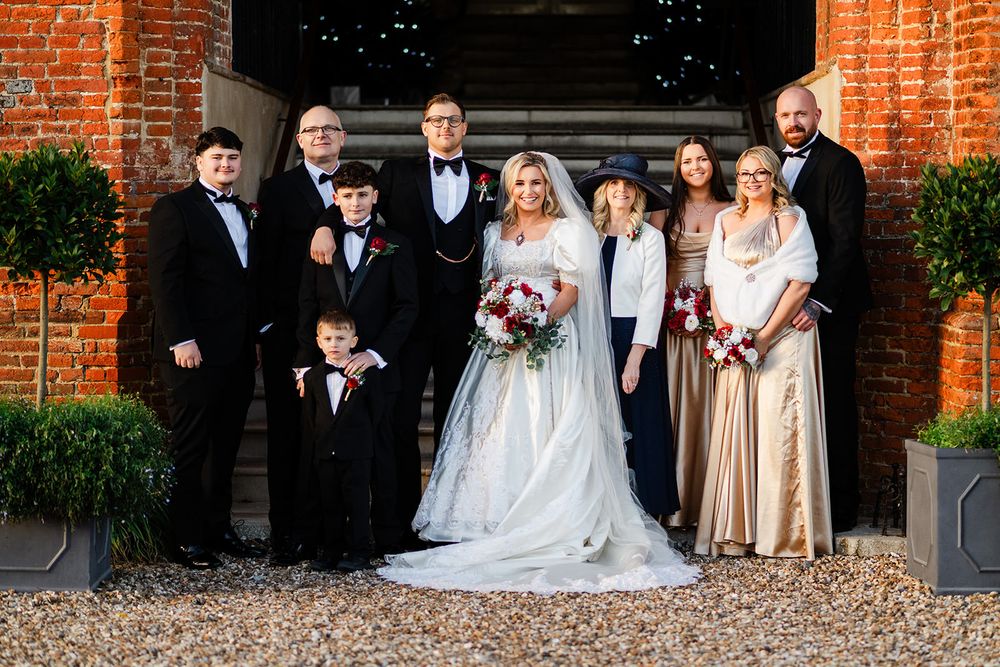 A wedding party poses for formal portraits outside a historic red brick building entrance.