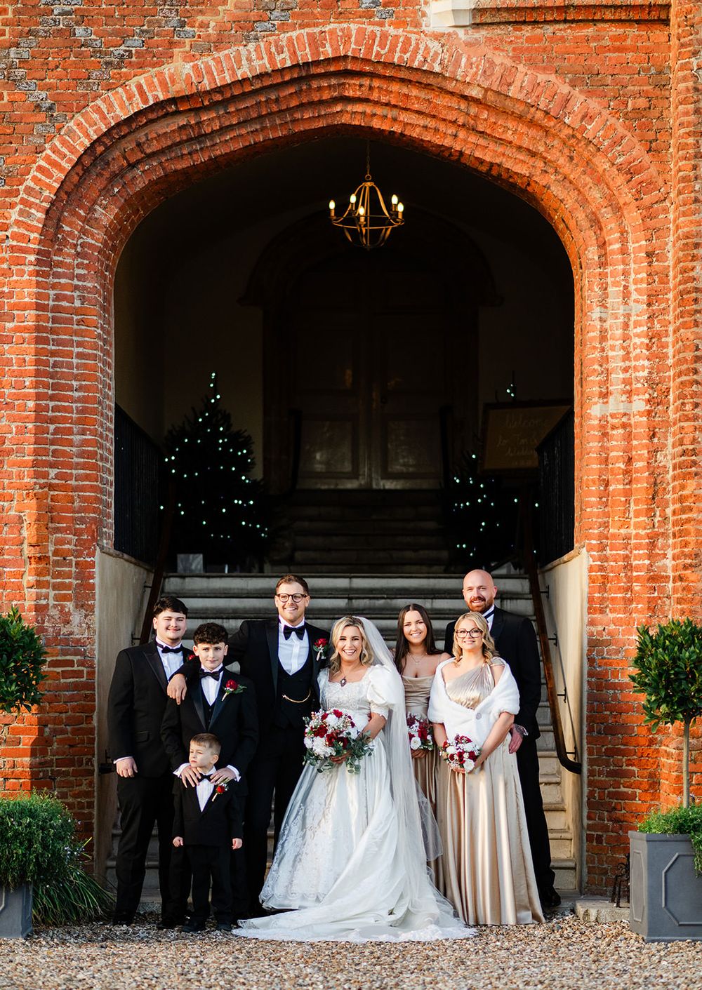 Wedding party stands in elegant brick archway venue during evening celebration.