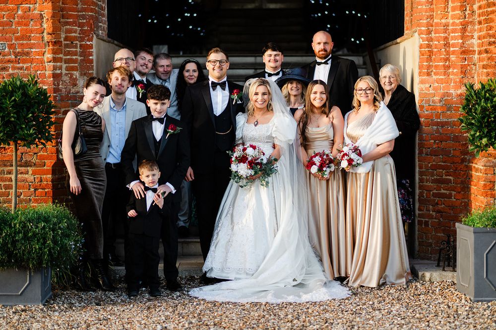 Wedding party poses together outside historic brick building with arched doorway in formal attire.