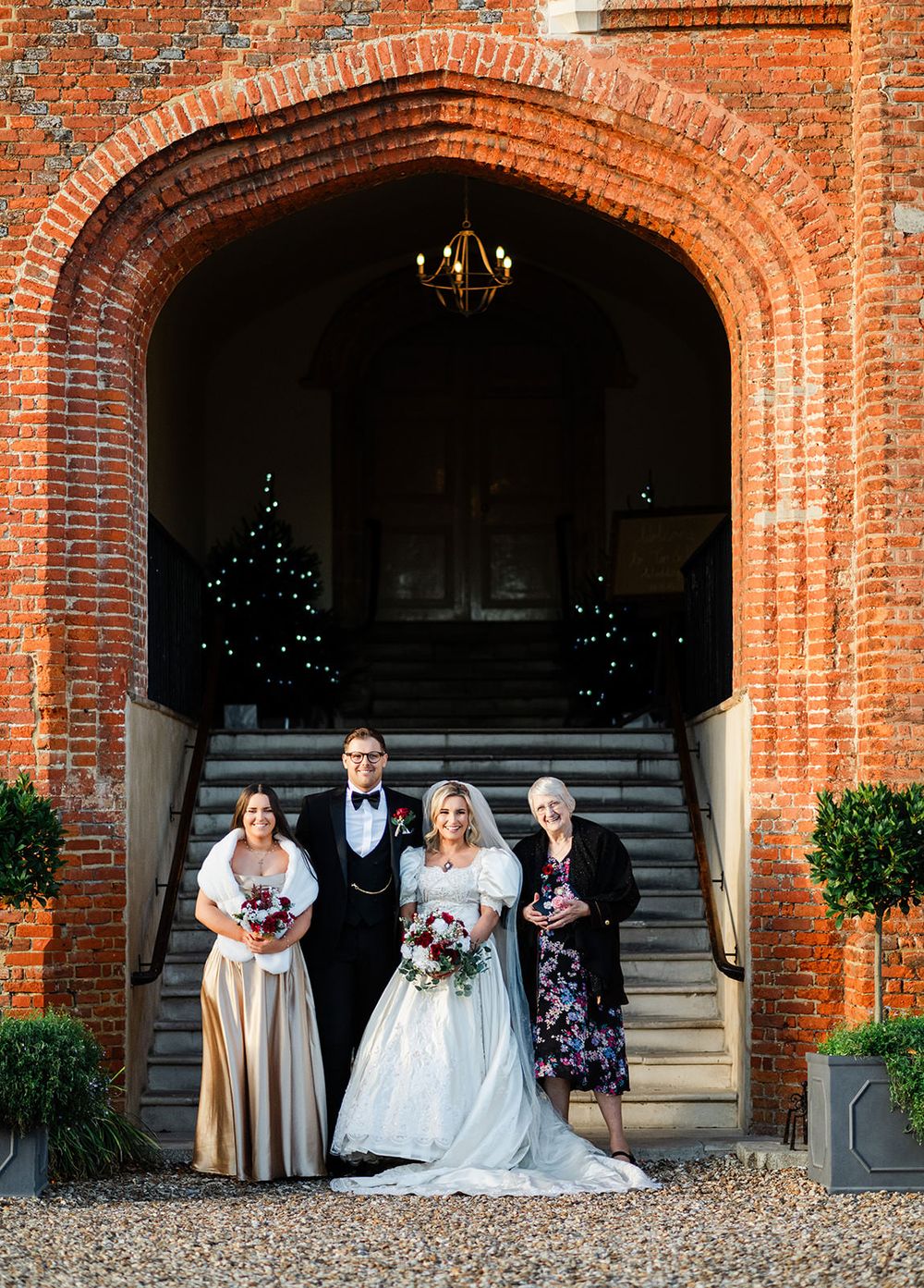 Wedding party poses under elegant brick archways at a historic venue during sunset celebration.