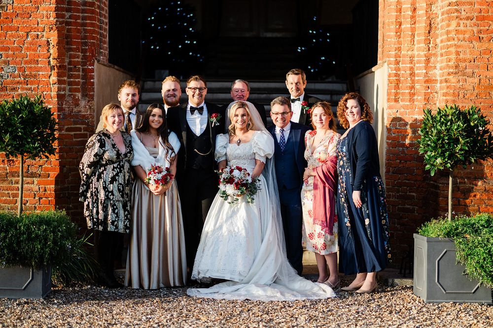 Wedding party poses in front of rustic brick columns at an elegant outdoor venue during sunset.