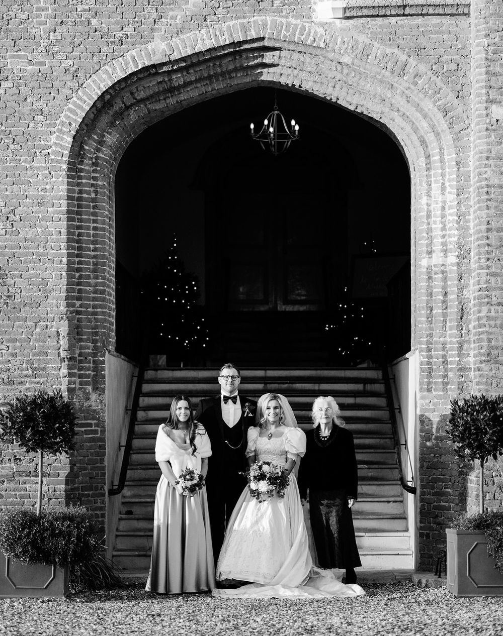 Black and white wedding party portrait in front of an elegant brick archway entrance.