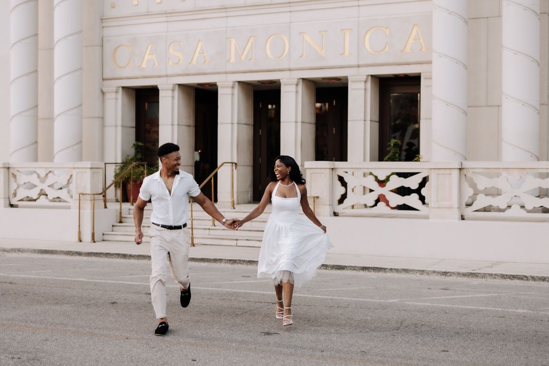 A couple shares a romantic moment while walking between elegant white columns of a historic building.