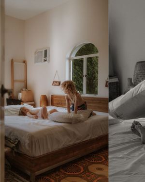 A cozy bedroom interior features natural light filtering through an arched window and wooden bed frame.