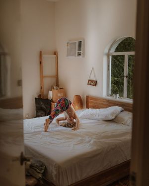 A bright bedroom with an arched window, wooden ladder, and white bedding captures a playful morning moment.
