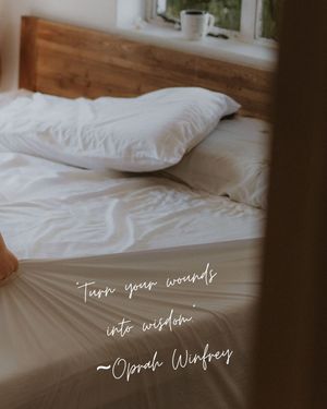 White unmade bed with wooden headboard and Oprah Winfrey quote overlay about wisdom.