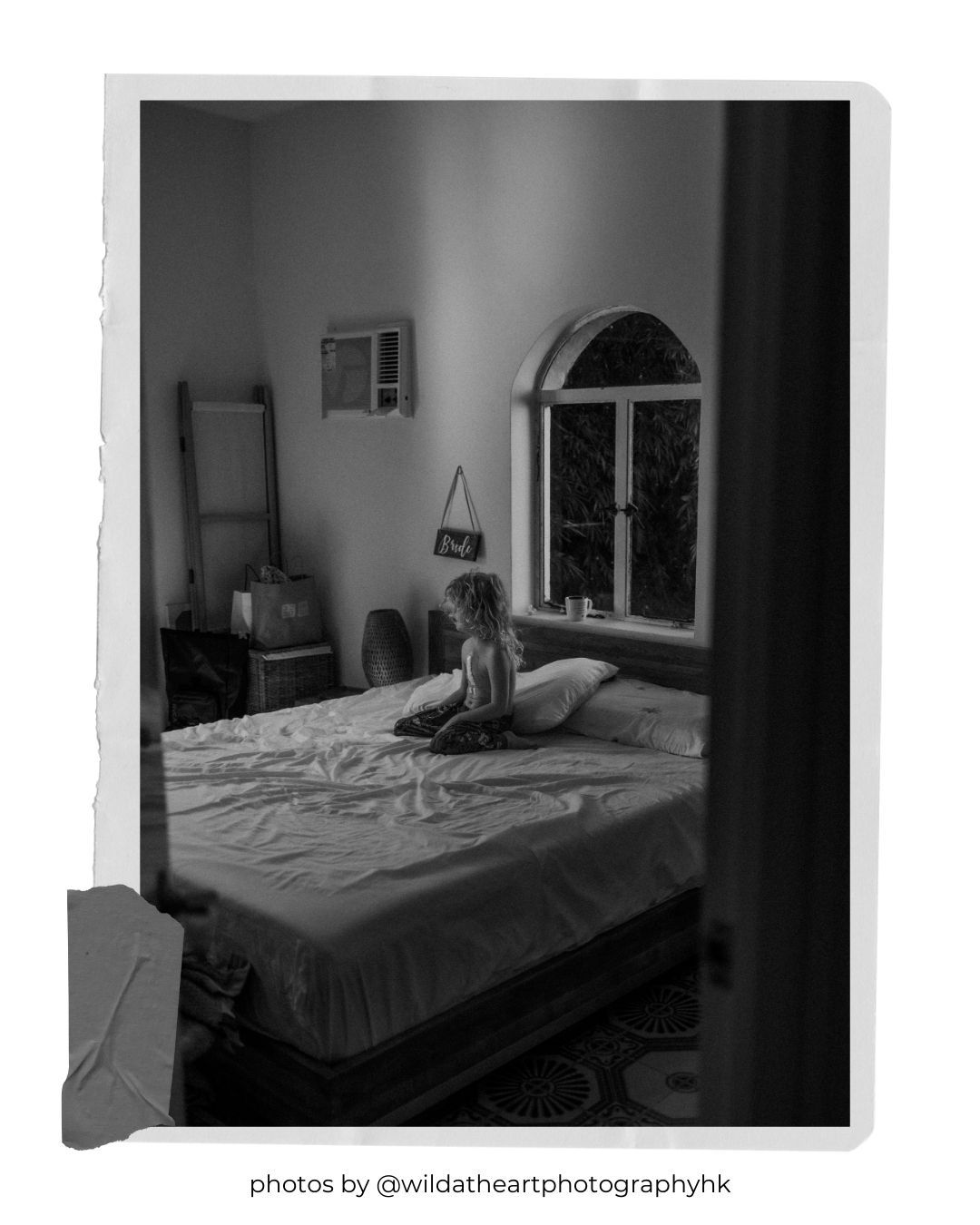 Black and white bedroom photo taken through doorway showing minimalist decor and arched window.