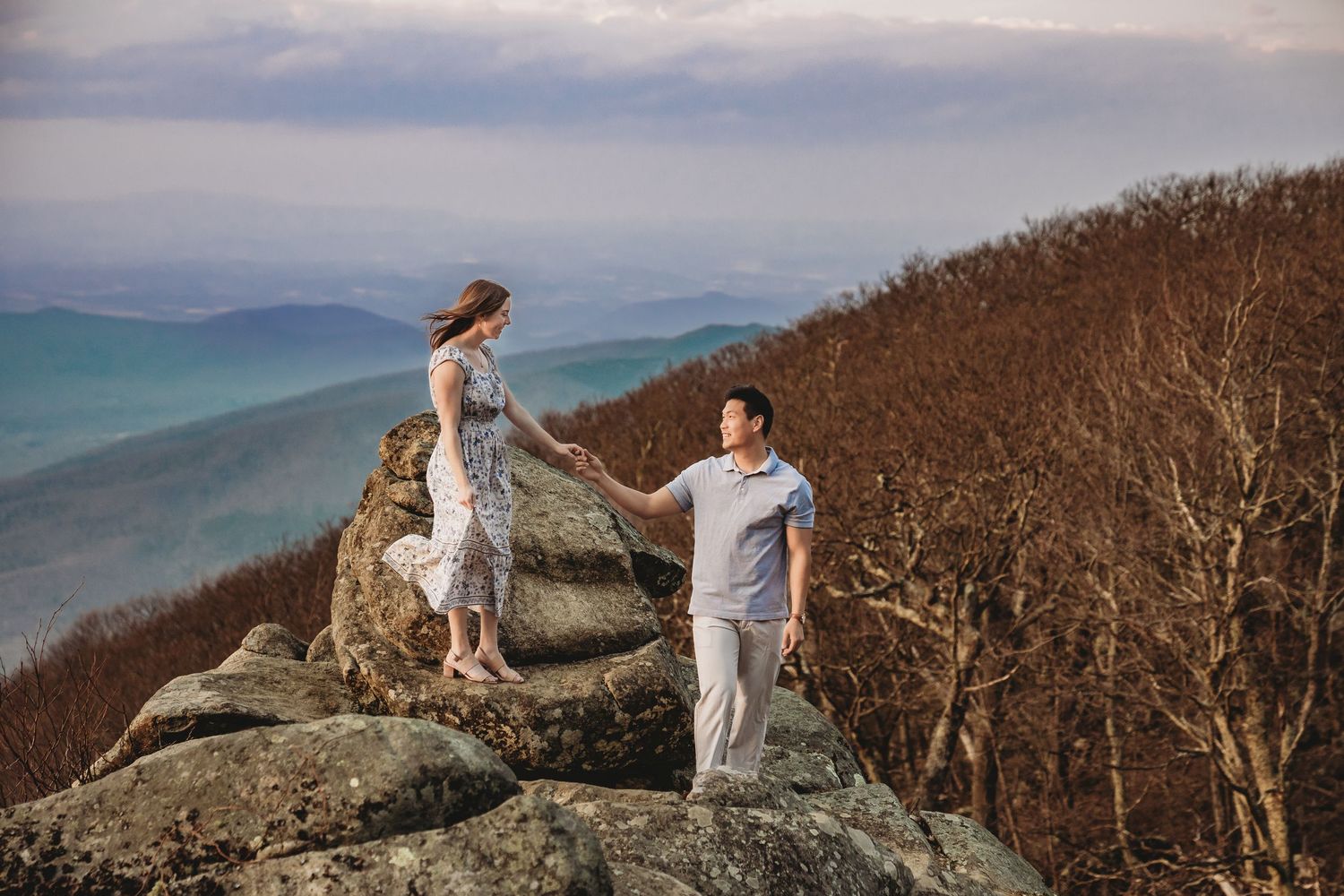 An adventurous couple poses on mountain peaks during sunset in the Blue Ridge Mountains.