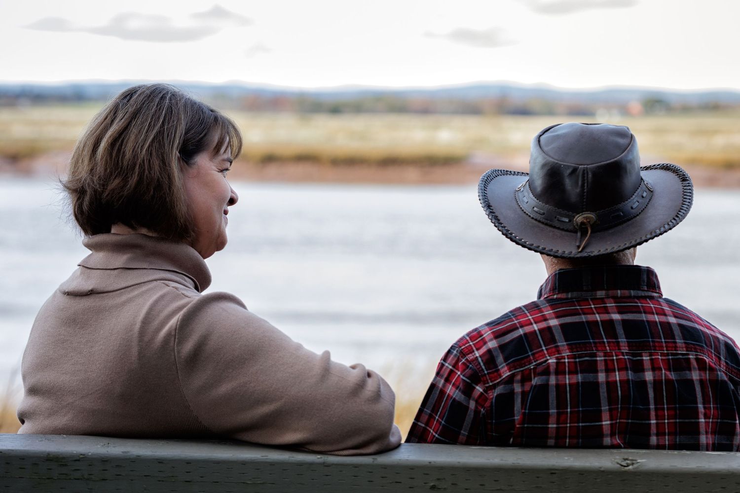 A couple in casual clothing sits together watching a scenic lake view at sunset.