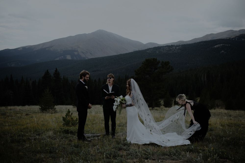 A wedding ceremony unfolds against dramatic mountain peaks at dusk.