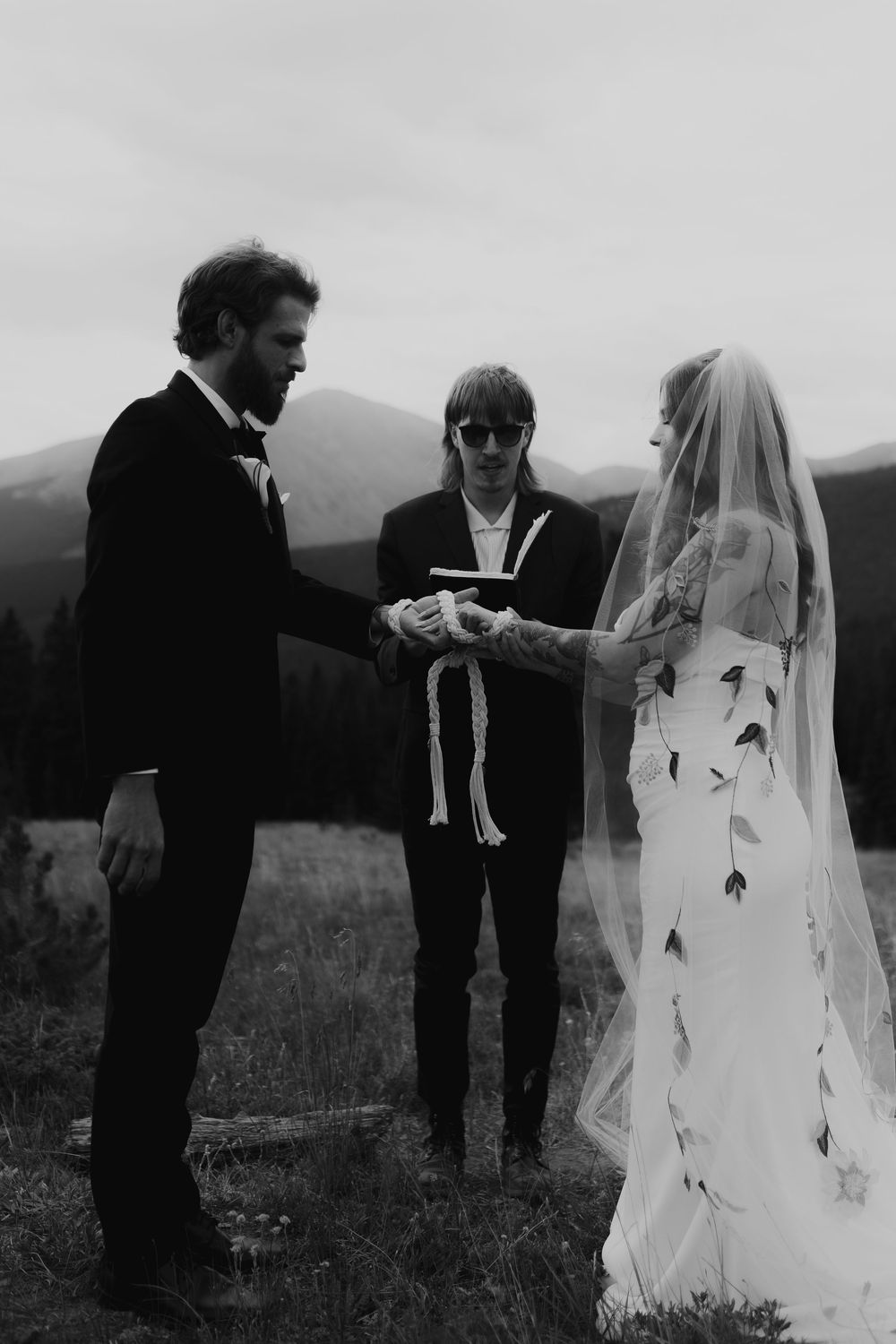 A black and white wedding ceremony takes place in a scenic mountain field.