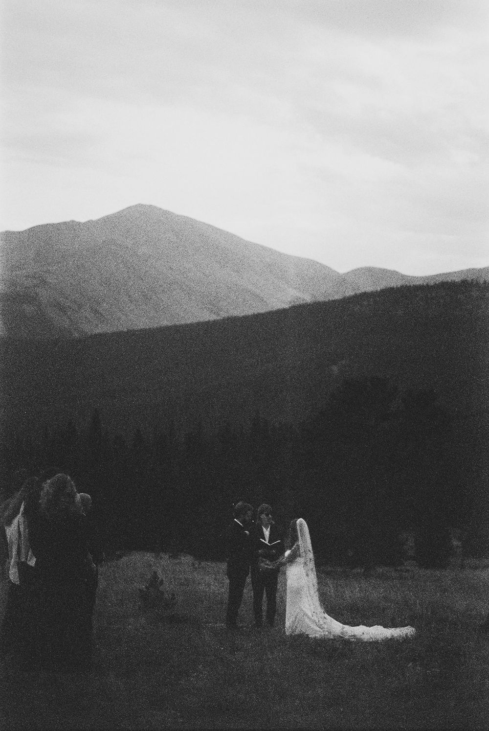 Silhouettes of a wedding party against dramatic mountain peaks at dusk.
