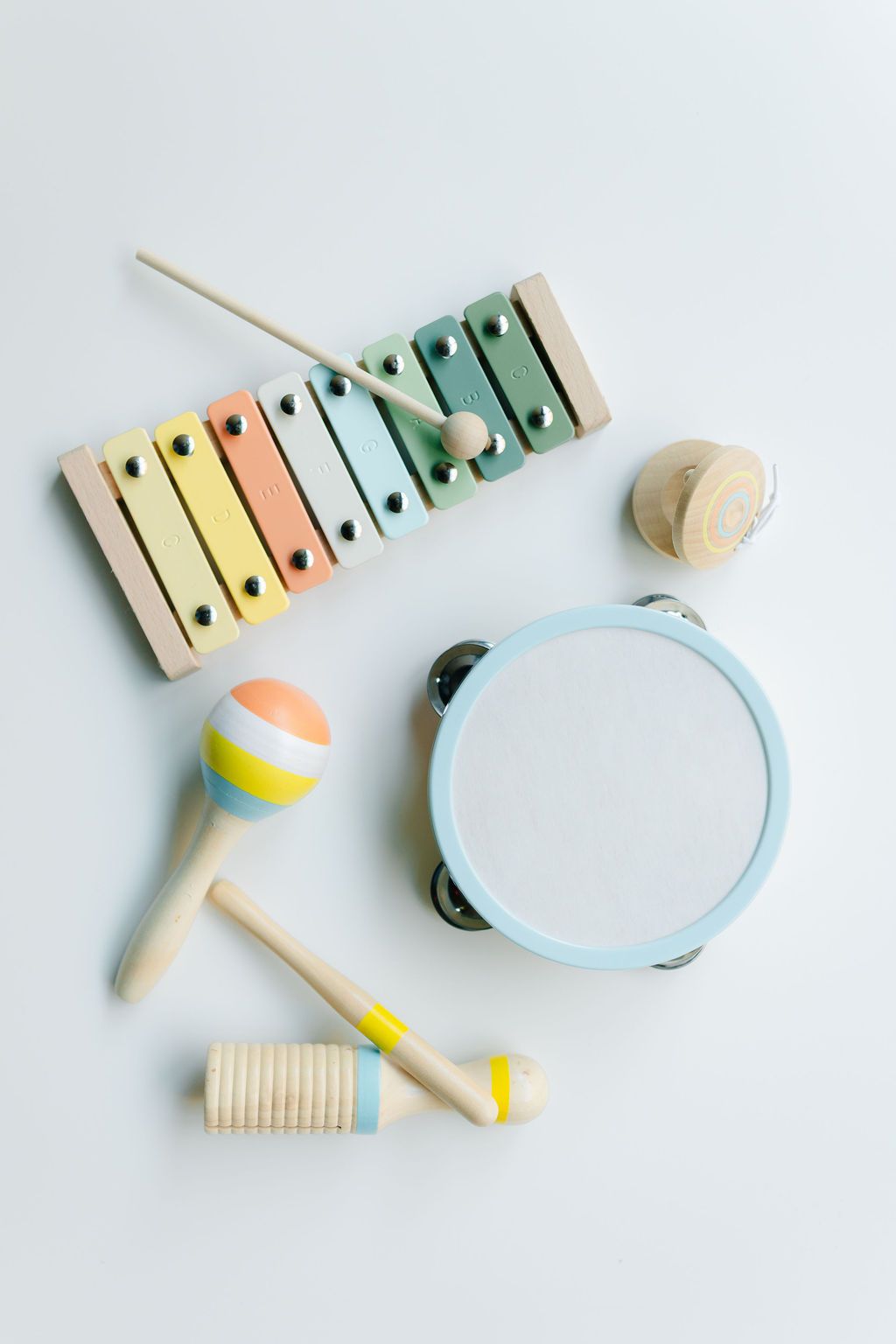 Pastel-colored montessori wooden musical toys including a xylophone, tambourine, and percussion instruments arranged on white background.