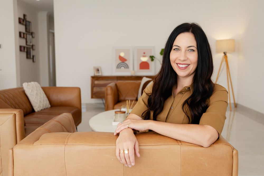 A person sits on a brown couch and smiles in a house to hire for photoshoot