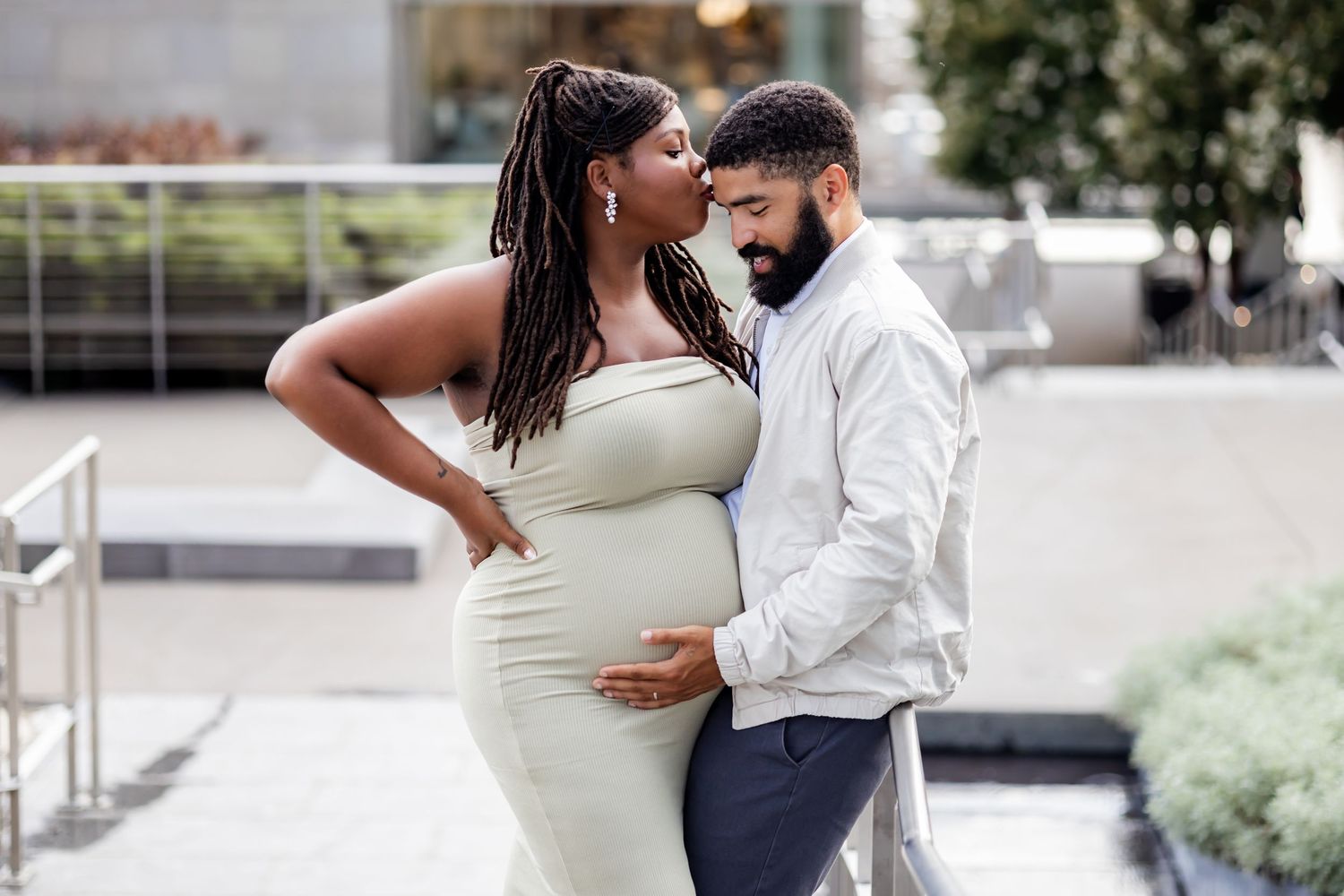 A couple embraces lovingly during a maternity photo shoot outdoors on a sunny day.