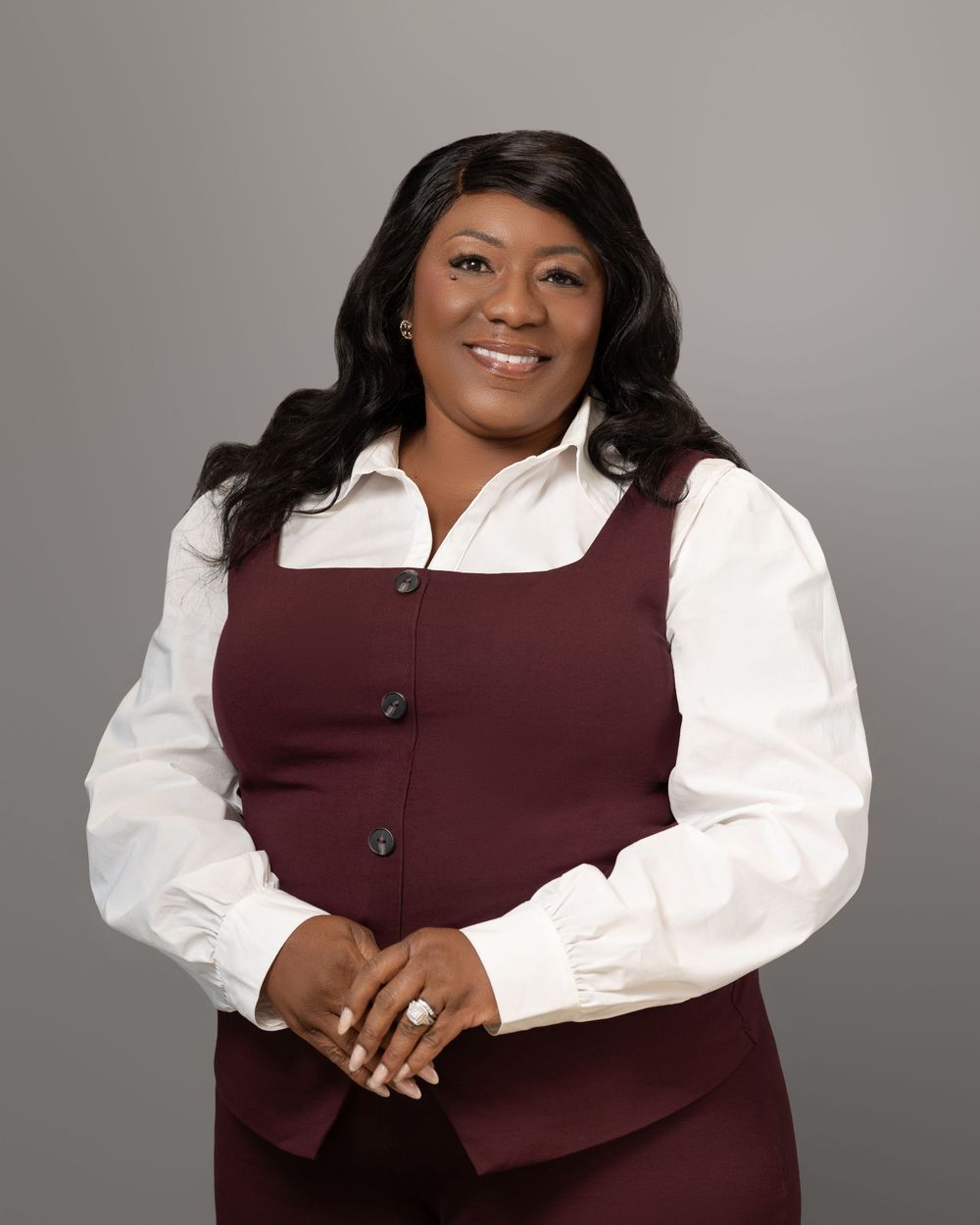Professional studio portrait of someone wearing a burgundy vest and white blouse against a gray background.