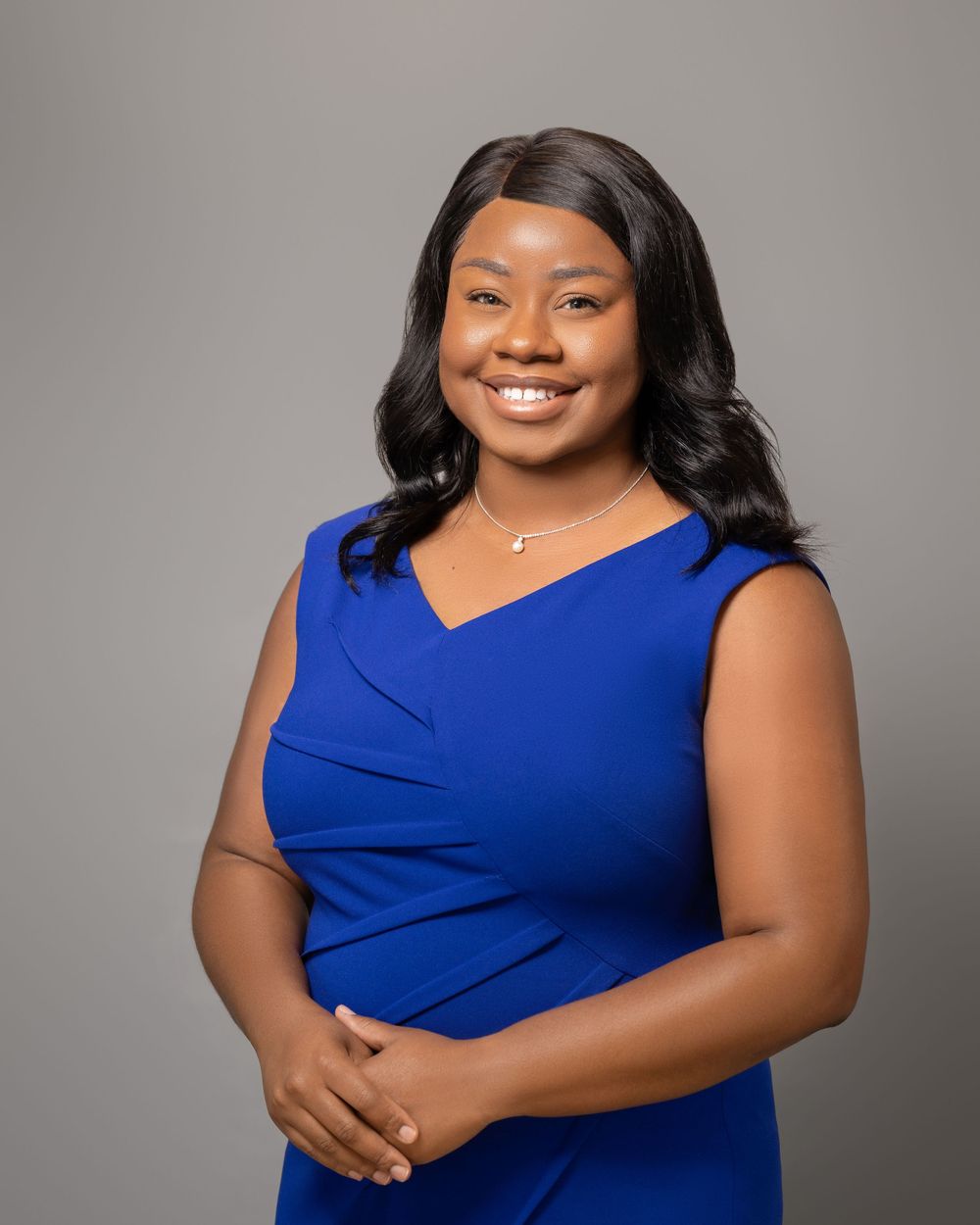 A person in a royal blue sleeveless dress poses against a gray studio backdrop.