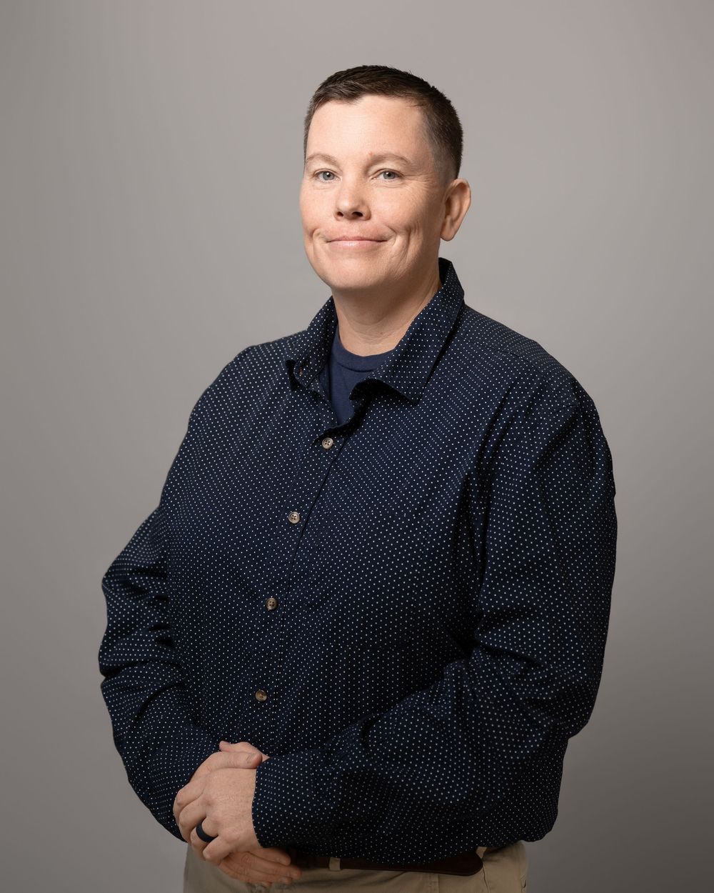 Professional studio portrait of someone in a navy polka dot button-down shirt against a neutral gray background.