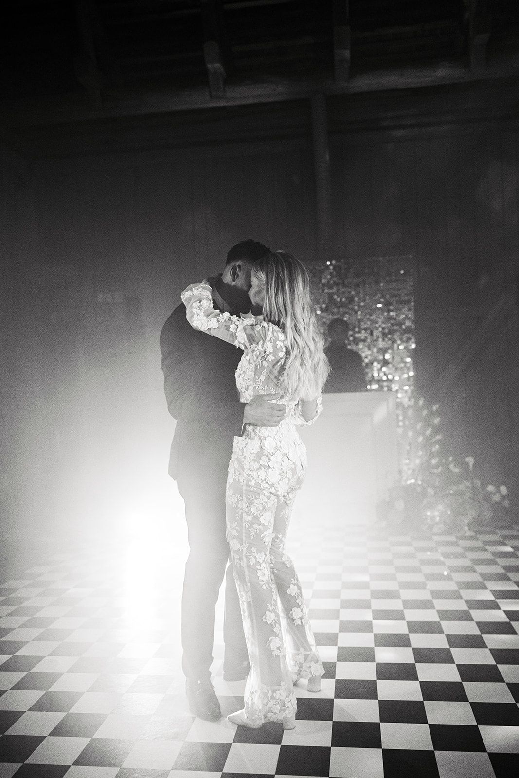 Silhouettes of people dancing on a black and white checkered floor with bright backlighting creating dramatic shadows.