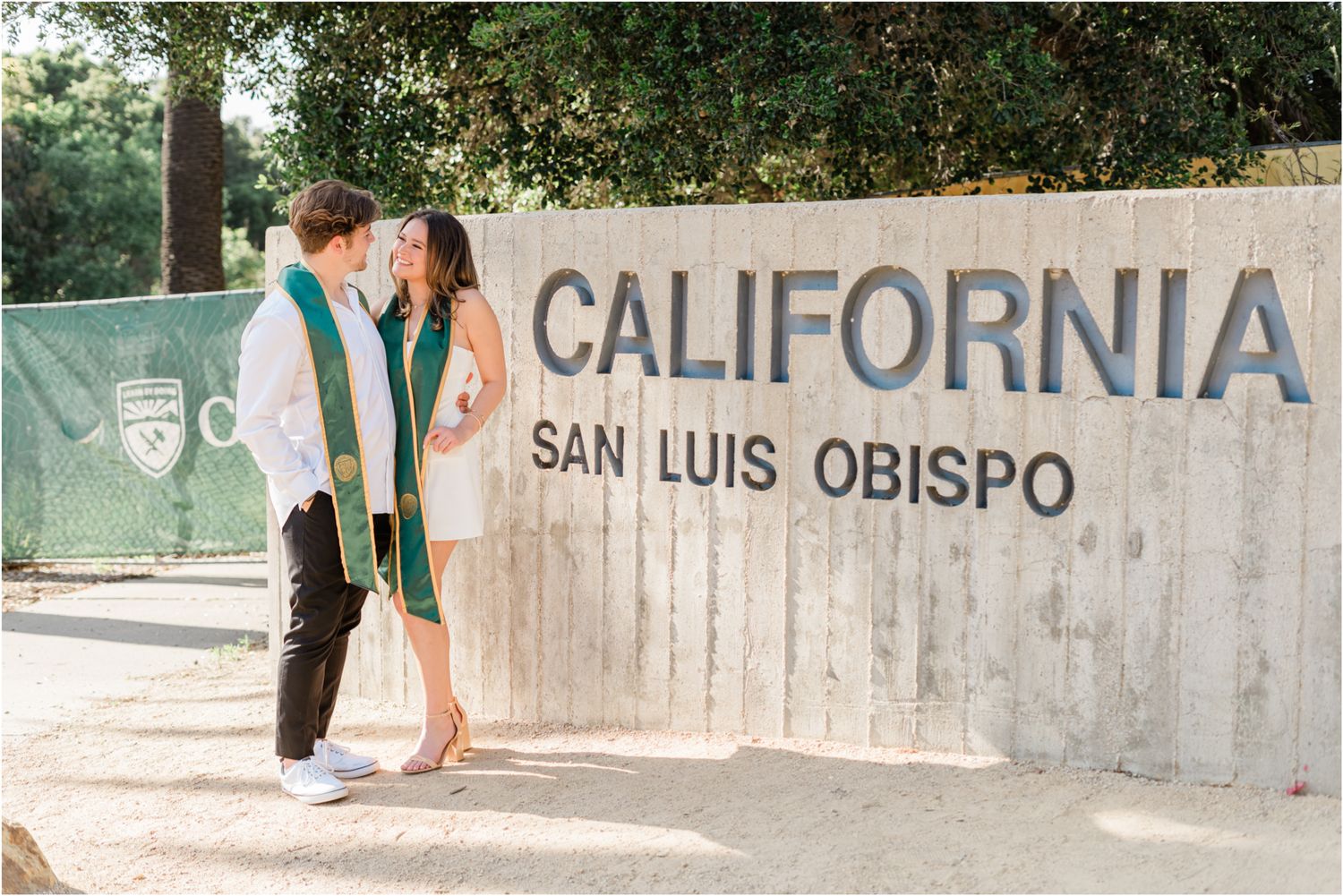 cal poly couple standing in front cal poly sign for grad photos during grad session at cal poly