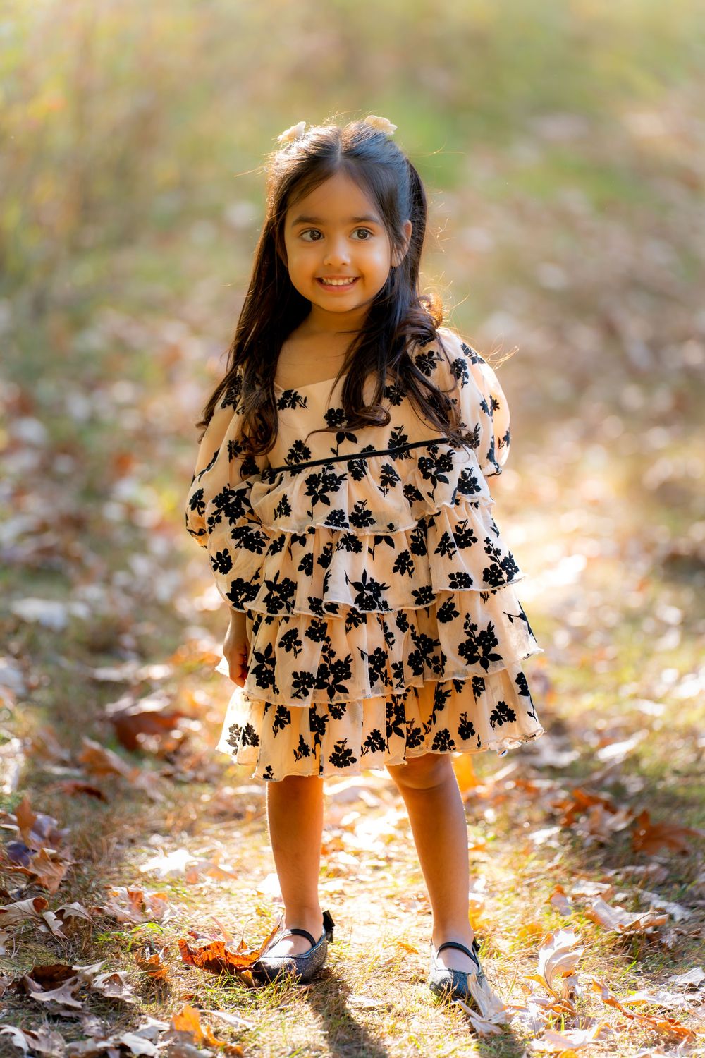 A pink and black floral dress is showcased in autumn leaves with warm golden lighting.