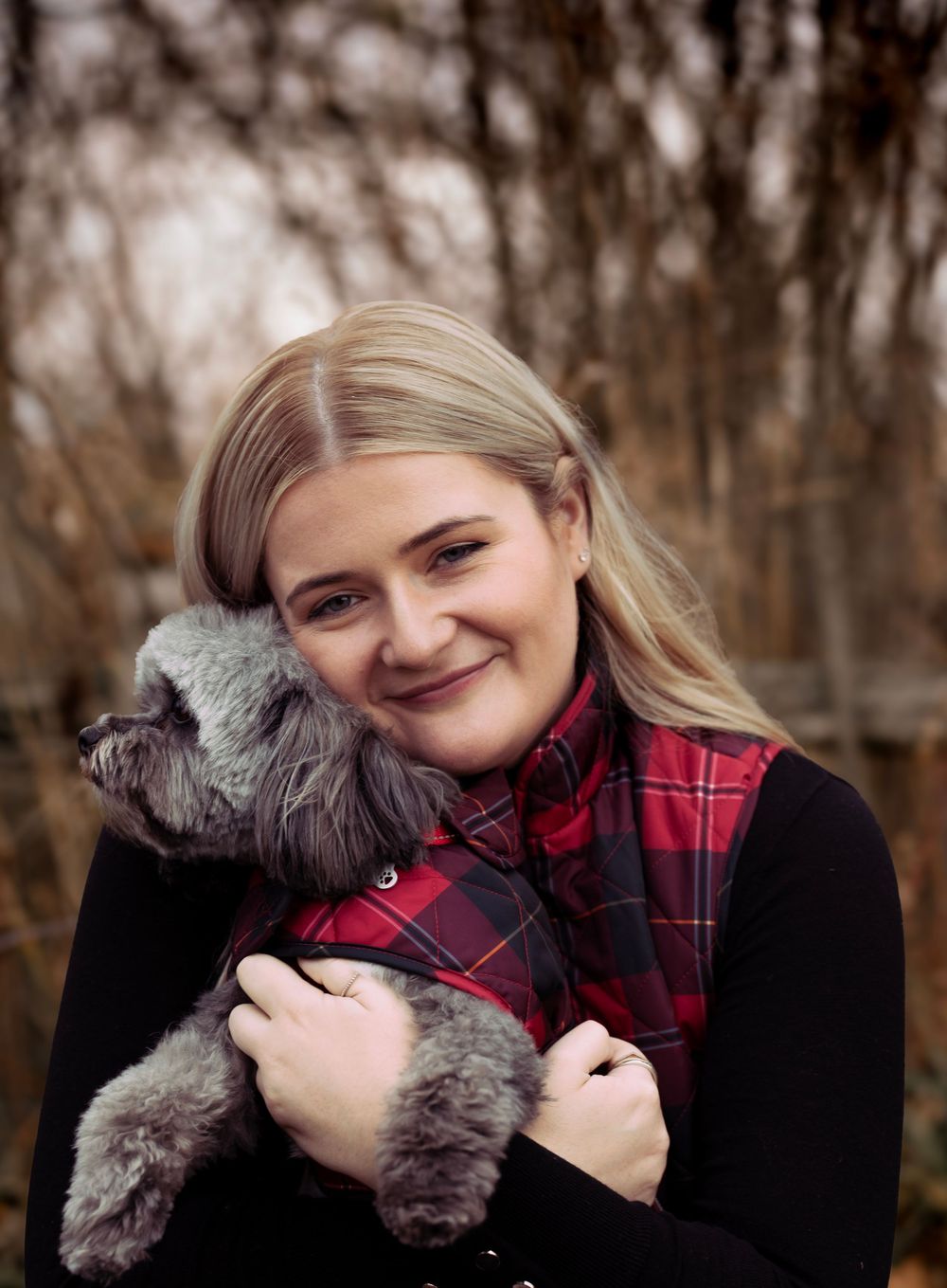Person in red plaid shirt hugging small grey dog during autumn photoshoot.