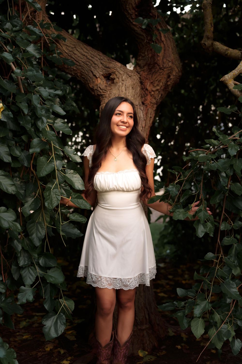 A white summer dress is showcased against a leafy backdrop in natural lighting.