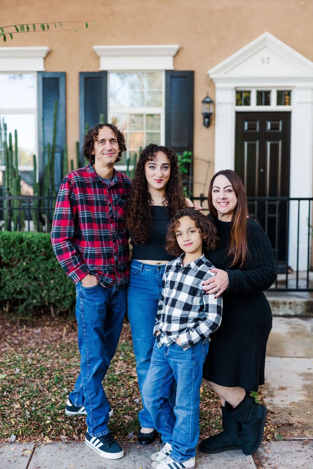 A group stands together on a porch wearing plaid and casual clothing in front of a white house entrance.