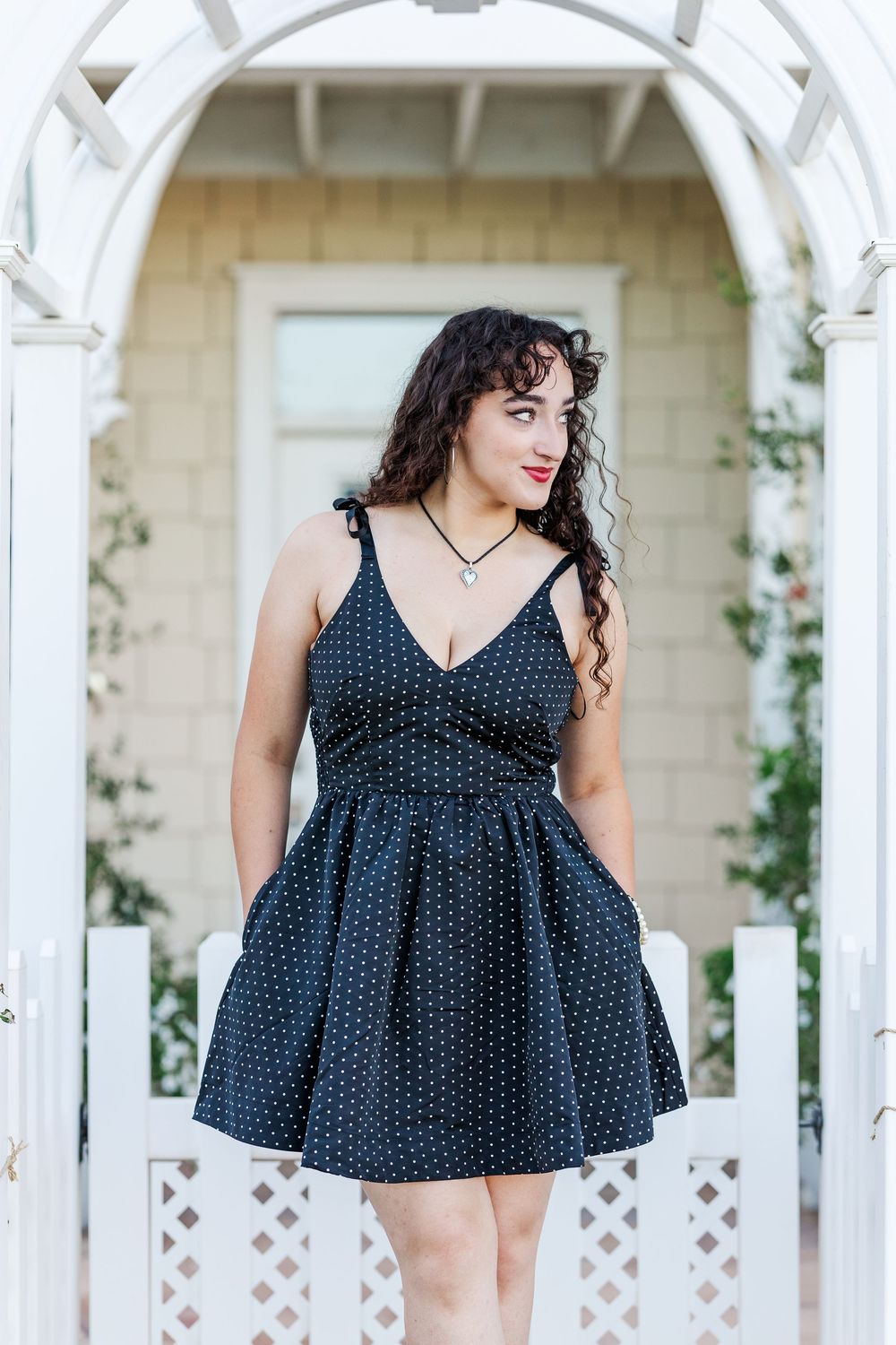A navy polka dot dress is showcased against white garden arches and lattice in summer sunlight.