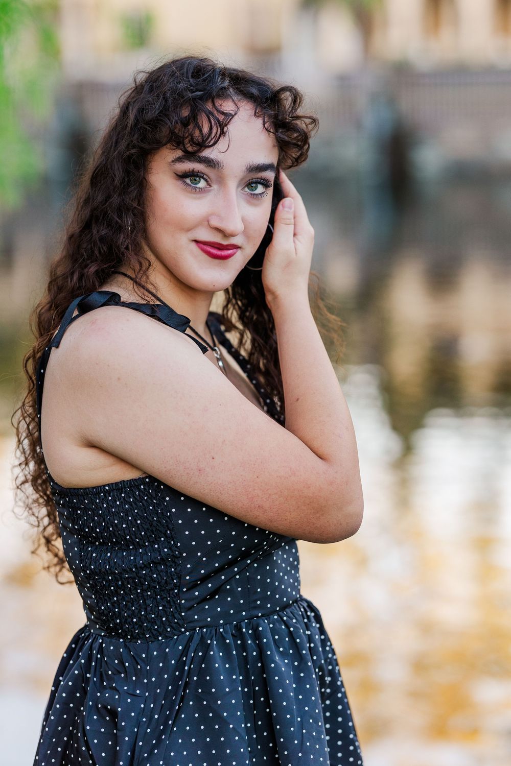A polka dot dress is worn during an outdoor photoshoot near a reflective pond.