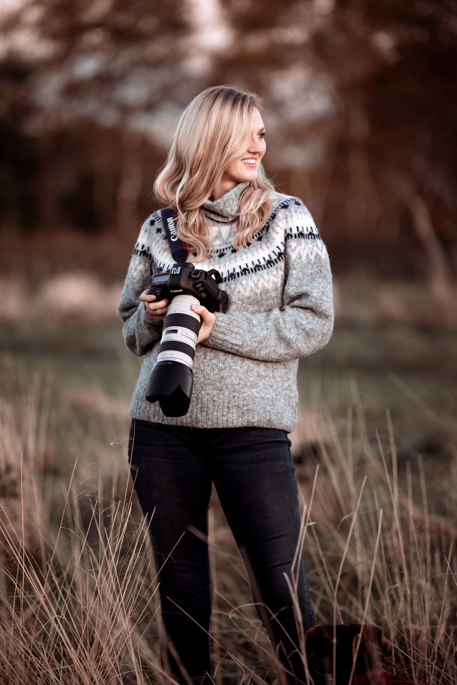 Photographer in cozy winter sweater holds professional camera equipment outdoors.