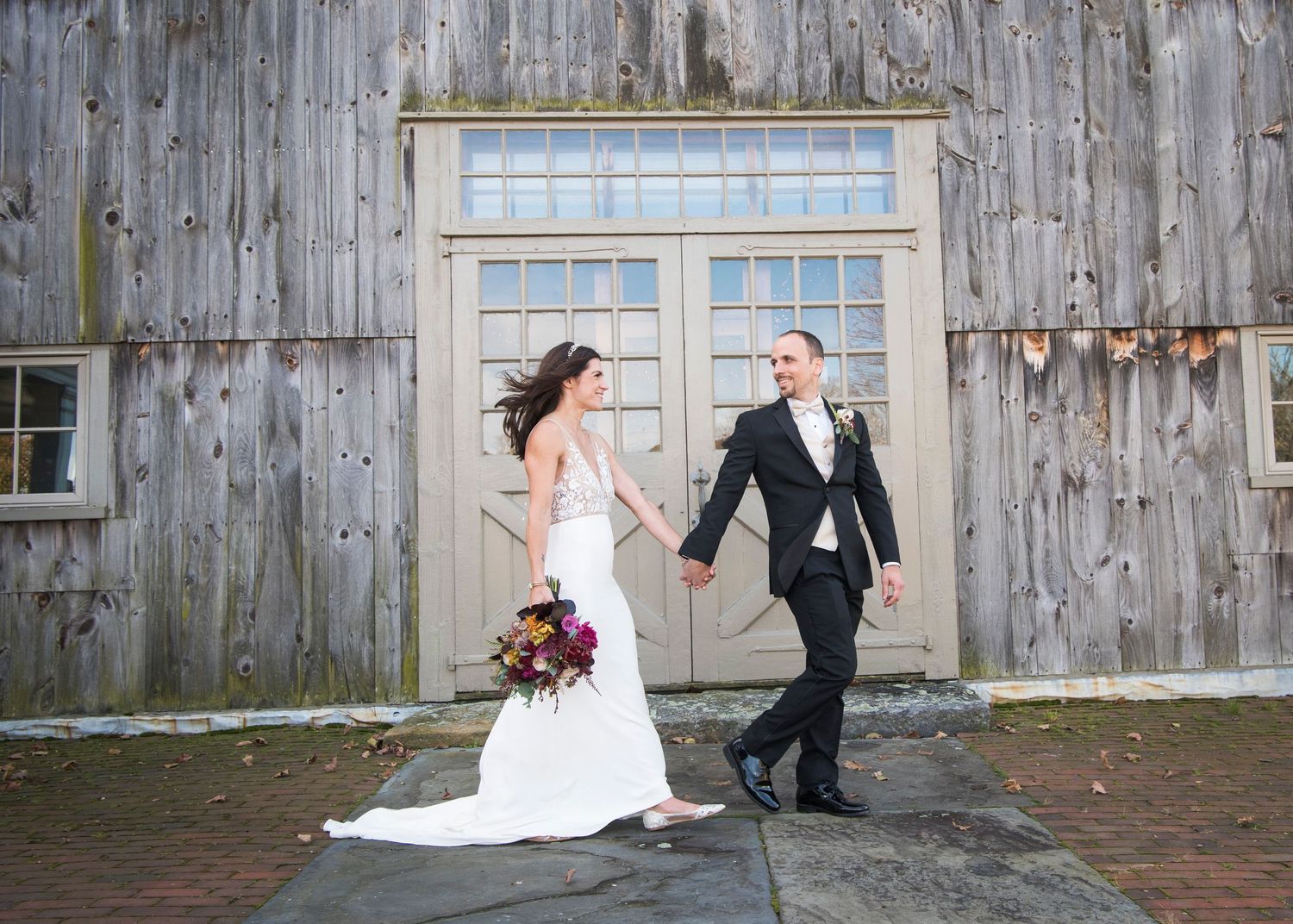 A rustic barn wedding venue with weathered wood siding and brick pathway leading to a central doorway.