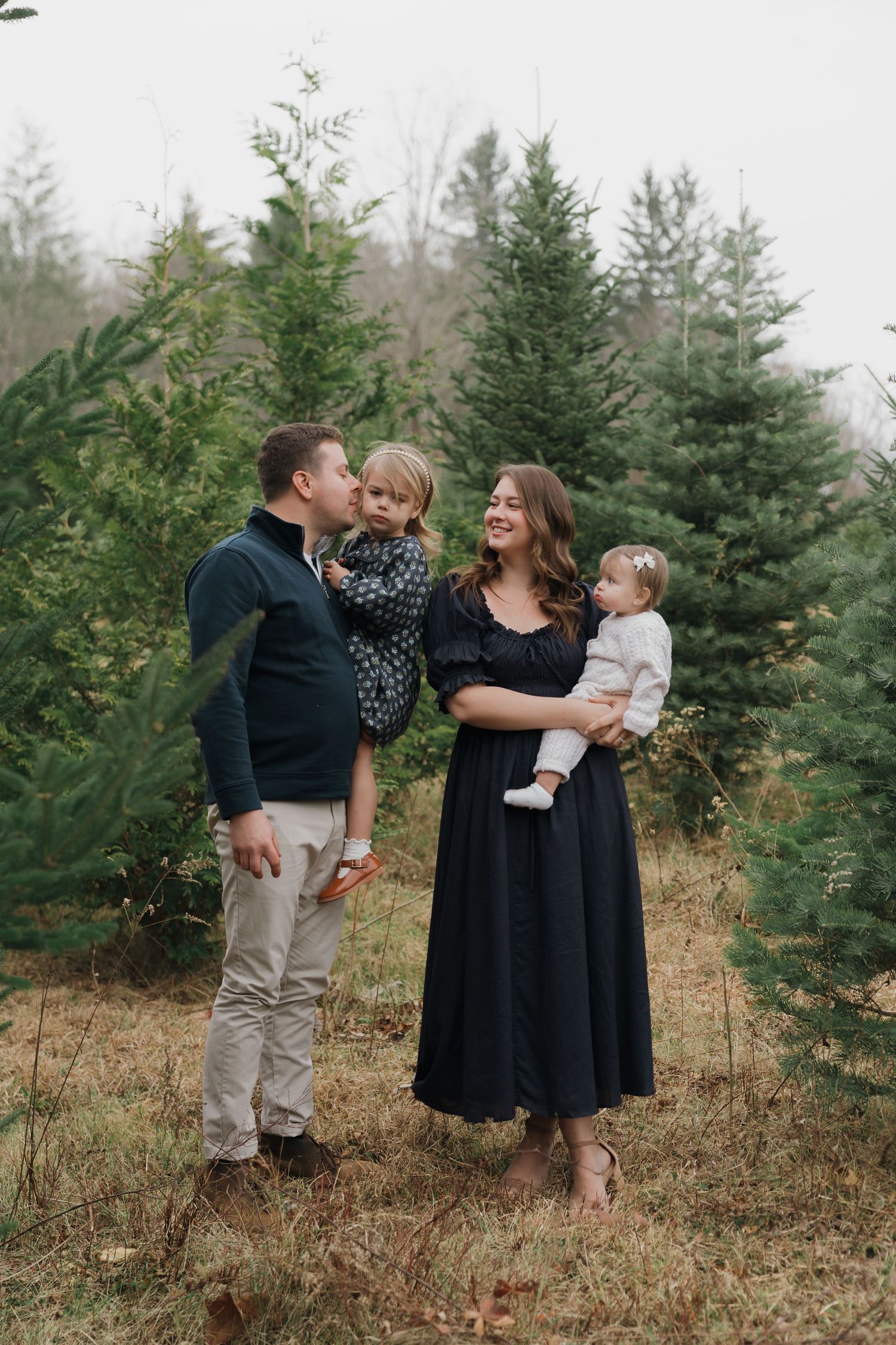 A family shares a joyful moment together among evergreen trees at a Christmas tree farm.