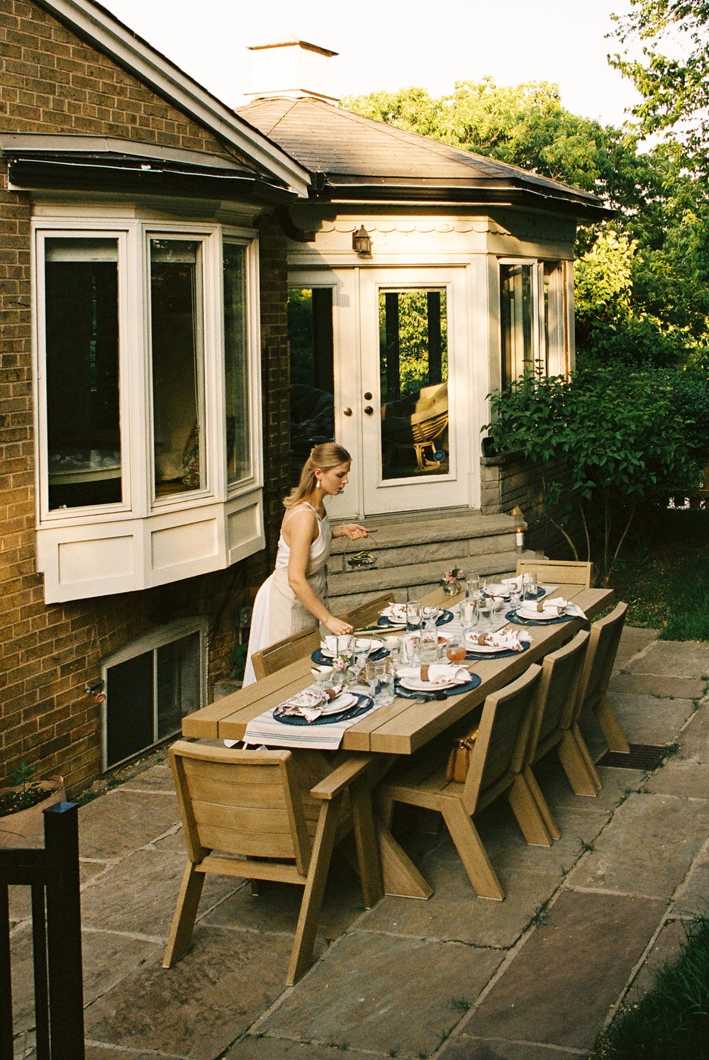 A series of four panoramic photos showing an outdoor dining setup with wooden benches against a brick house at sunset.
