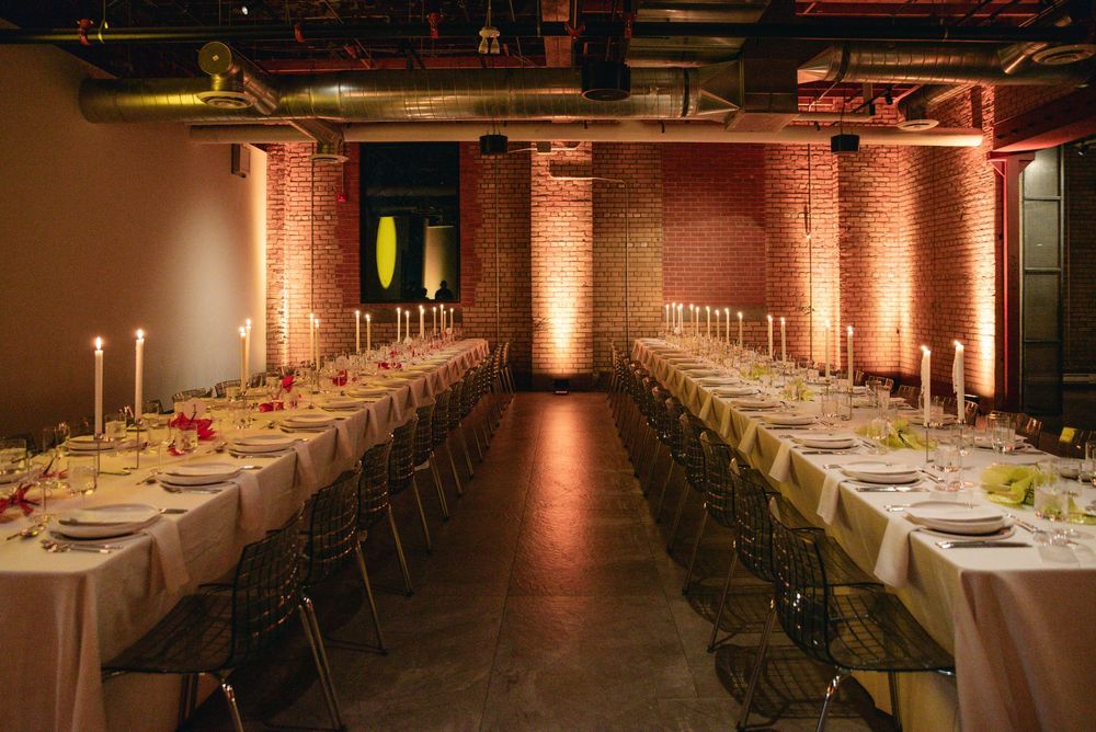 Elegant banquet hall with long white-clothed tables, candlesticks, and warm uplighting on exposed brick walls.