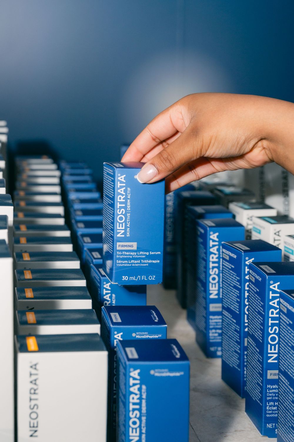 A row of blue medical product boxes being arranged on a shelf with a hand reaching to adjust one box.