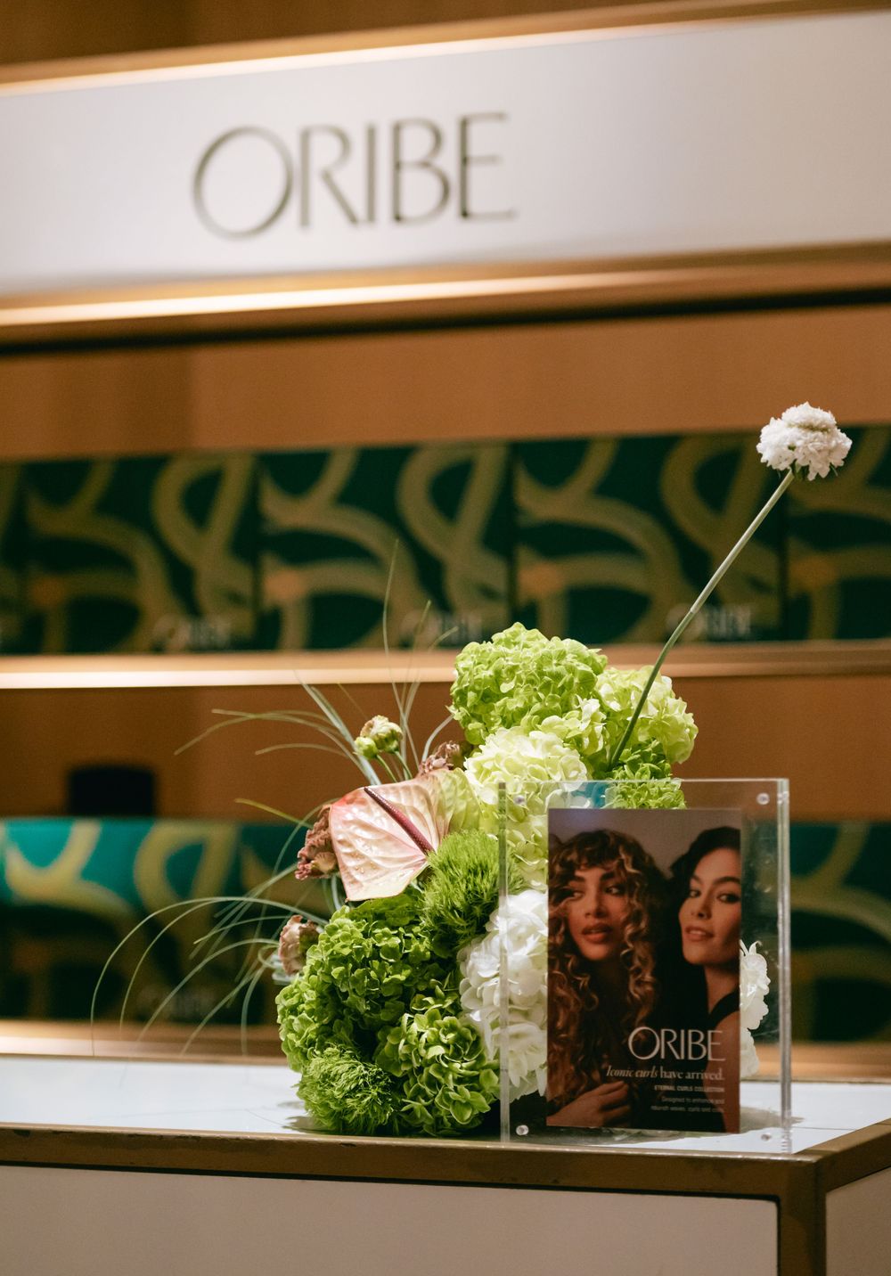 Elegant display of Oribe beauty products and floral arrangements with green hydrangeas on a sleek table setting.