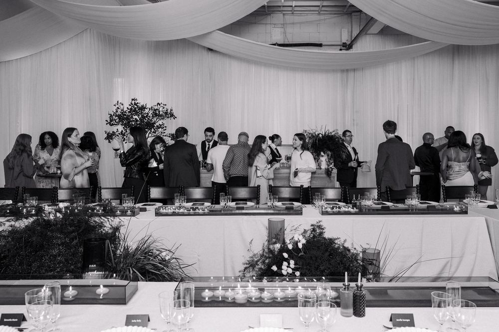 Black and white photo of wedding reception guests mingling at a buffet table under elegant draped white fabric ceiling.