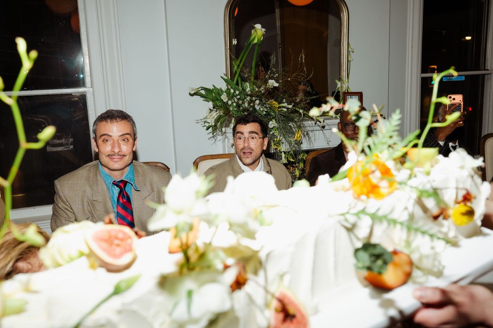 Two men smiling at a elegantly decorated wedding reception table with floral centerpieces and white flowers.