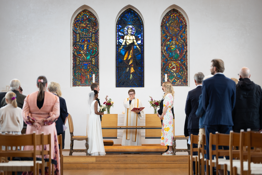 Brudepar ved alteret i kirke med fargerike vinduer, bryllupsseremoni fotografert av Prospectxmedia.