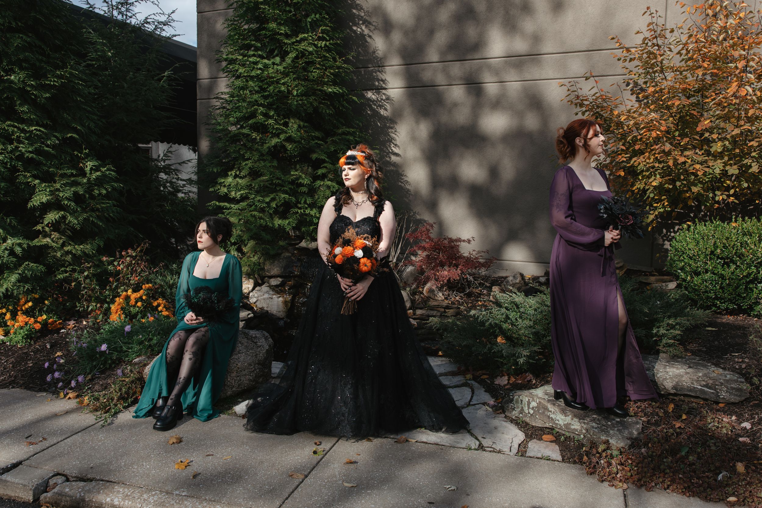 A wedding party poses in a garden setting with autumn foliage and stone walls creating an elegant outdoor backdrop.